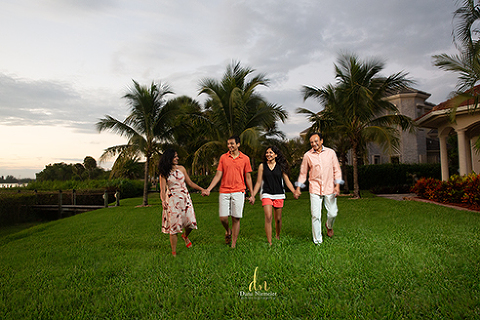 Family walking hand in hand laughing toward camera very green grass coconut palms in background and cloudy blue grey sky